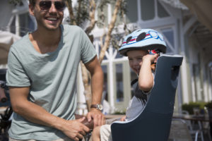 Enfant sur un siège vélo avec un casque et son père à côté