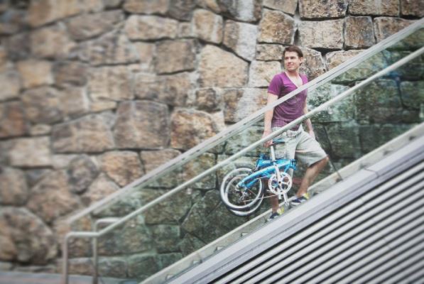 Homme portant un vélo pliant dans des escalators