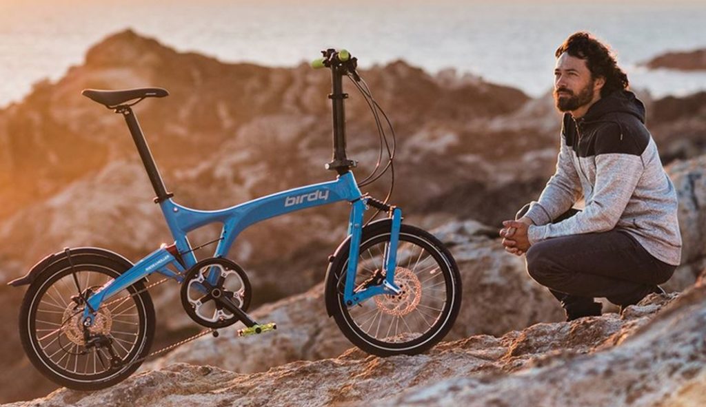 Homme accroupi près d'un vélo pliant bleu