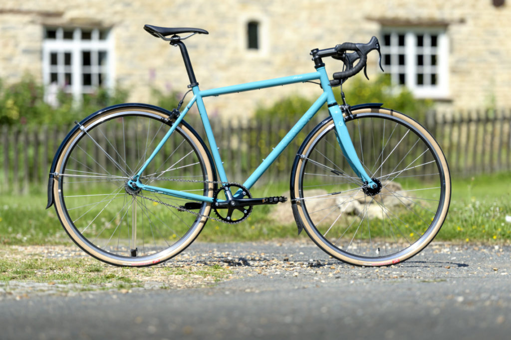 Vélo gravel Genesis Flyer 2018 bleu devant une maison de pierre