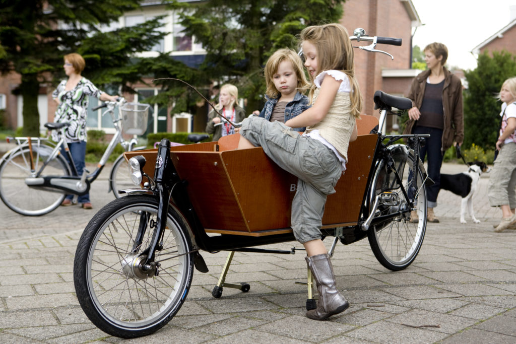 Enfant montant seule dans la caisse d'un vélo cargo à deux roues