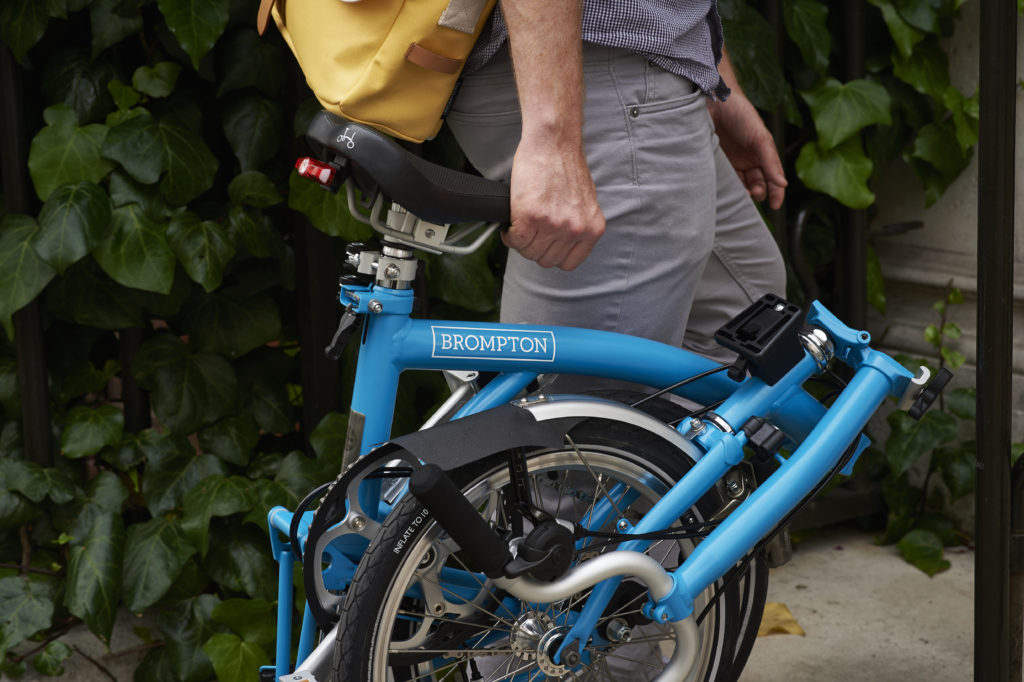 Cycliste qui porte son vélo pliant Brompton plié par la selle