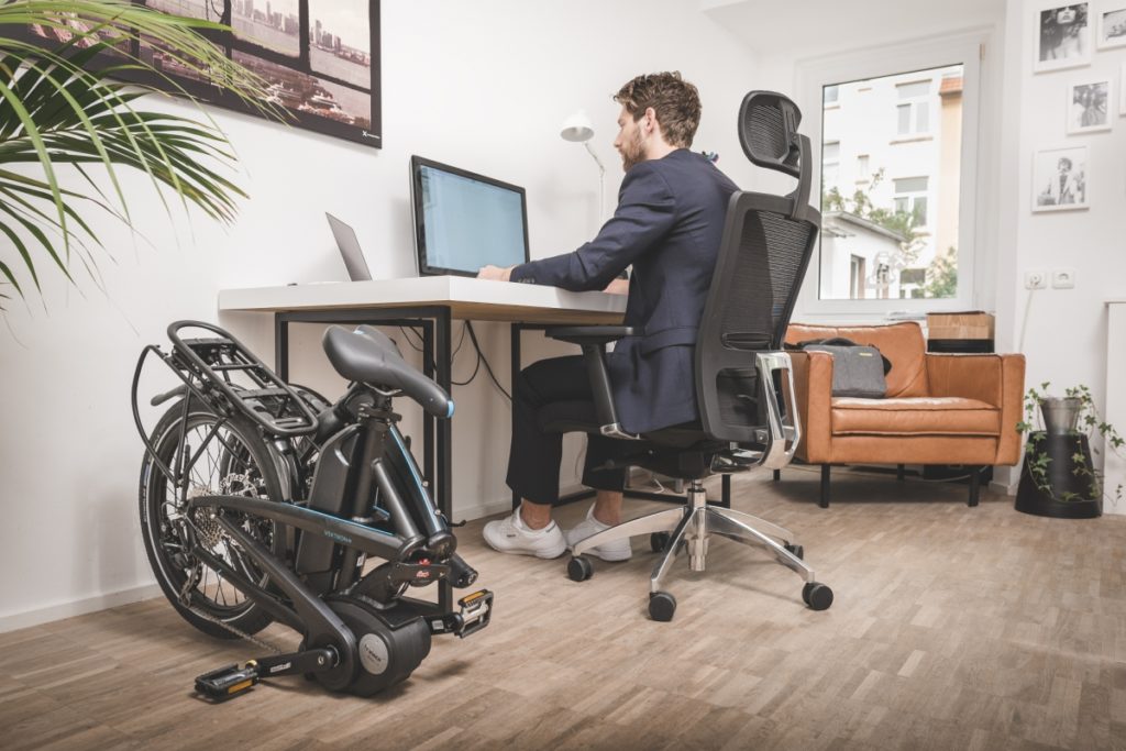 Homme travaillant à son ordinateur avec son vélo pliant plié à côté de son bureau