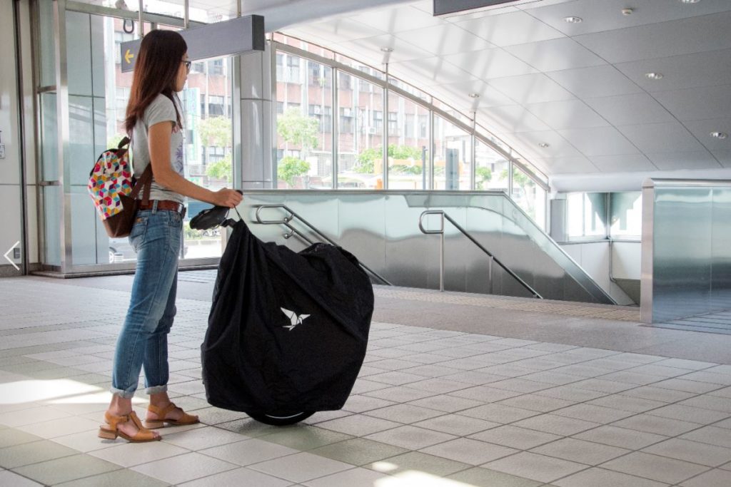 Femme poussant son vélo pliant replié et dans son sac de transport