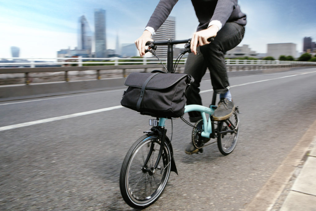 Vélo pliant électrique Brompton Go en train de rouler en ville avec sacoche avant