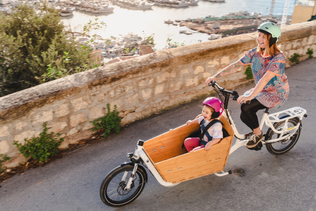 Cycliste sur son vélo cargo avec sa fille, toutes deux souriantes