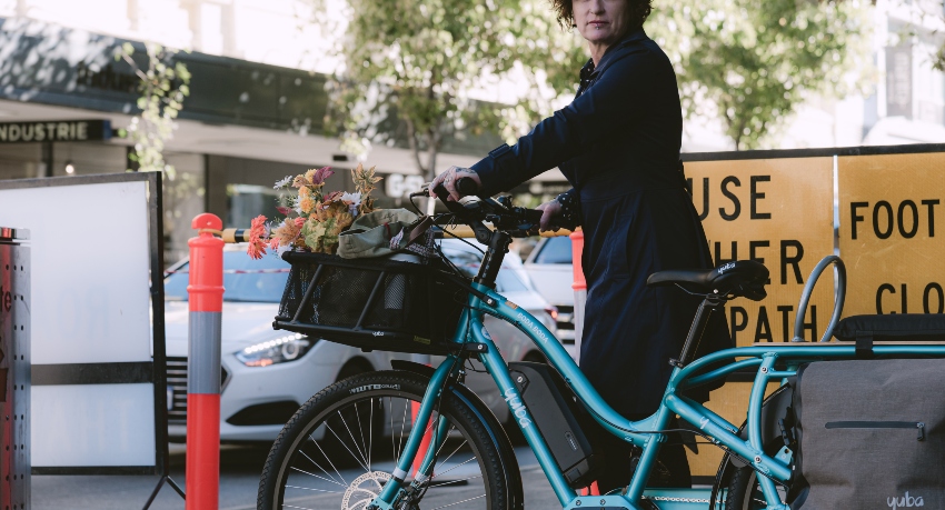 Femme marchant à côté de son vélo cargo chargé avec panier et sacoches