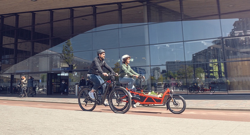 Femme en bi-porteur et homme en vélo électrique circulant en milieu urbain 