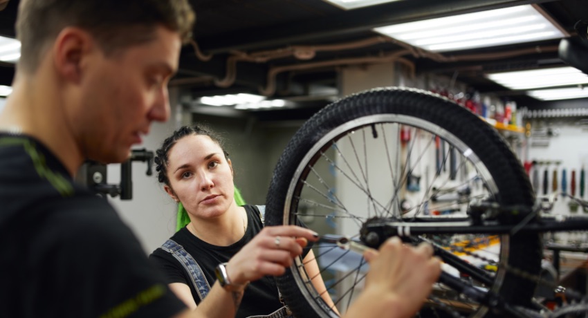 Une mécanicienne et un mécanicien en train de réparer une roue de vélo dans un atelier
