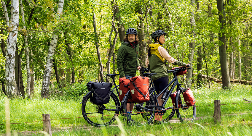 Un couple de cycliste équipé de sacoches latérales arrêté sur un chemin forestier.