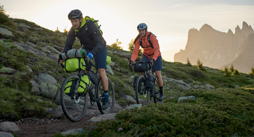 Un homme et une femme évoluent sur un sentier de montagne avec une configuration mixte bikepacking et cyclotourisme.