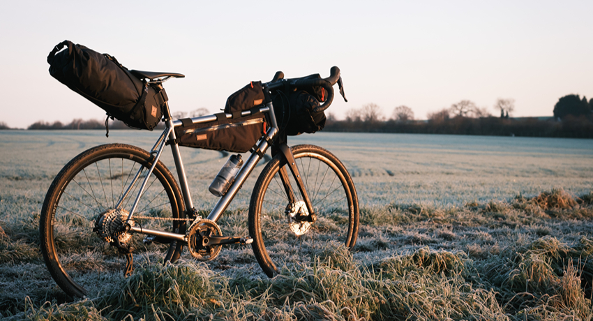 Un vélo de gravel équipé de 3 sacoches bikepacking Restrap dans un champ recouvert de givre.