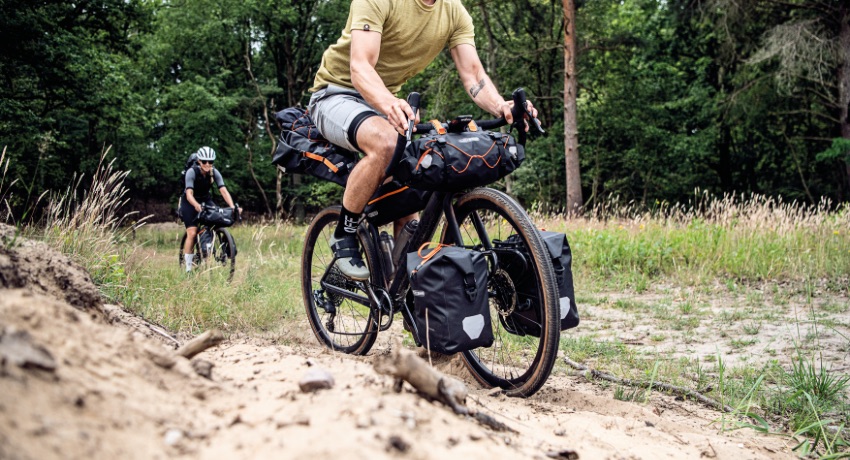 Un cycliste évoluant sur un chemin forestier avec une configuration mixte, bikepacking et sacoches latérales avant
