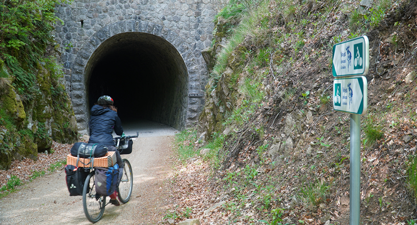 Une cycliste équipée pour l'itinérance s'apprête à pénétrer dans un des tunnels ferroviaires déclassés de la Dolce Via, en Ardèche.