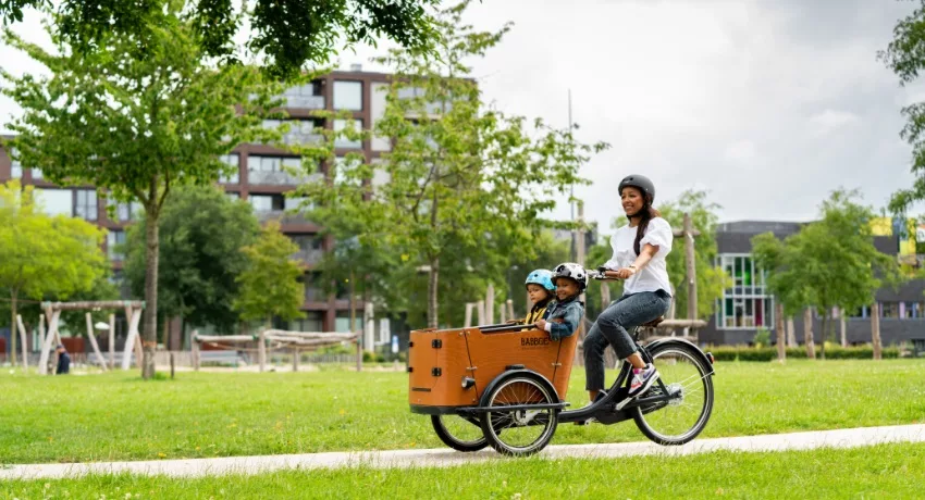 Une mère et ses deux enfants traversent un environnement urbain à bord d'un triporteur Babboe.