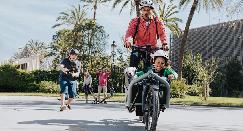 Un père en biporteur avec son fils et son chien évite de justesse un skateboard dans un parc grâce au système de freinage ABS de chez Bosch.