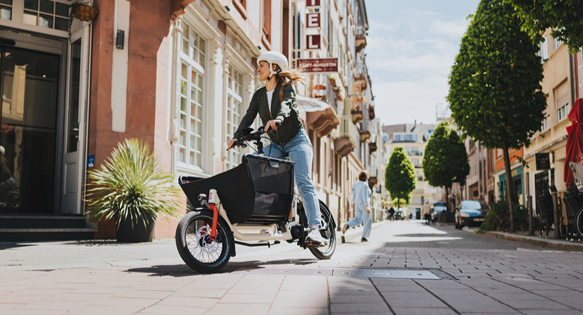 Une femme sur un biporteur compact amorce un virage dans une zone résidentielle urbaine.