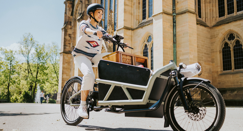 Une femme sur un biporteur chargé de petit mobilier file devant une église.