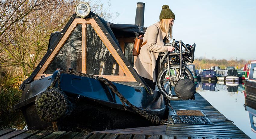 Une femme sort d'une péniche avec un vélo pliant à la main.