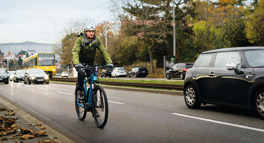 Un homme en vélo électrique sur une rocade à deux voies à forte fréquentation
