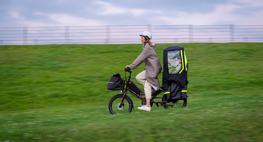 Un enfant à l'arrière d'un vélo rallongé Tern Quick Haul équipé d'une tente de pluie.