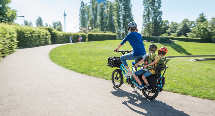 Une femme et deux enfants sur un vélo rallongé roulant sur une voie cyclable à l'écart des voitures.