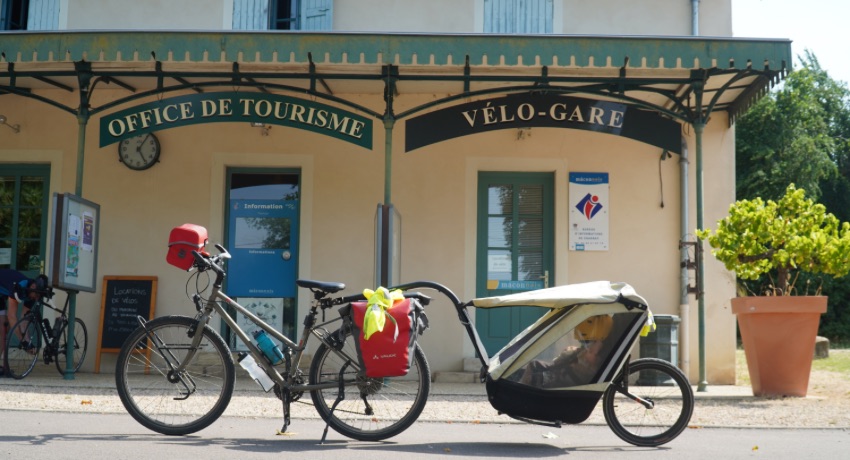 Un vélo de voyage et une remorque pour enfant devant une vélo-gare