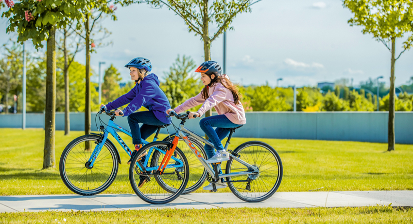 Une jeune fille et un jeune garçon roulant côte à côte sur une piste cyclable.