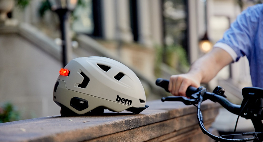 Un casque de cyclistes avec une lumière rouge à l'arrière posée sur le rebord d'un mur près d'un guidon de vélo.