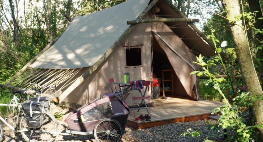 Un vélo de voyage et un remorque pour enfant stationnés devant une cabane de trappeur.