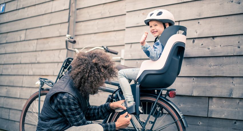 Un père attache les cale-pieds de sa fille installée sur un siège vélo enfant arrière.