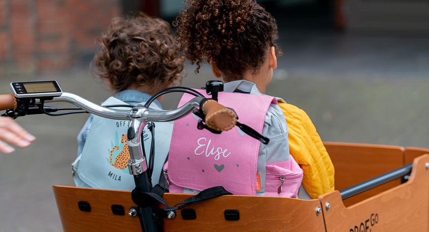 Deux petites filles de dos avec des sacs d'école installées dans la caisse d'un triporteur Babboe.