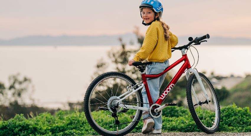 Une jeune fille avec un caque bleue observe la mer appuyée sur son vélo woom Original équipé de vitesses.