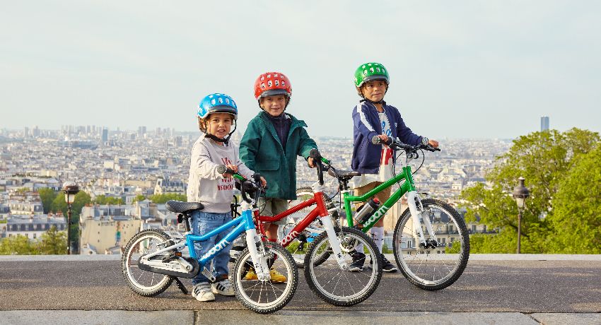 Trois enfants à côté de leur vélo woom Original bleu, rouge et vert.