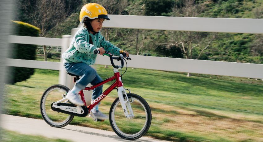 Une petite fille avec un casque jaune file sur un chemin de campagne au guidon d'un vélo woom Original.