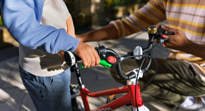 La main d'un enfant sur le levier de frein vert de son vélo woom Original.