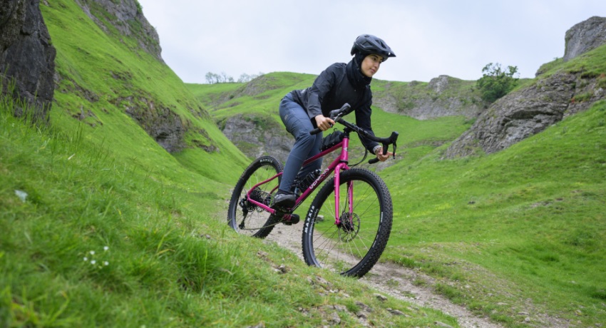 Une cycliste dévale une montagne verdoyante et escarpée au guidon du nouveau monstercross Genesis Vagabond.