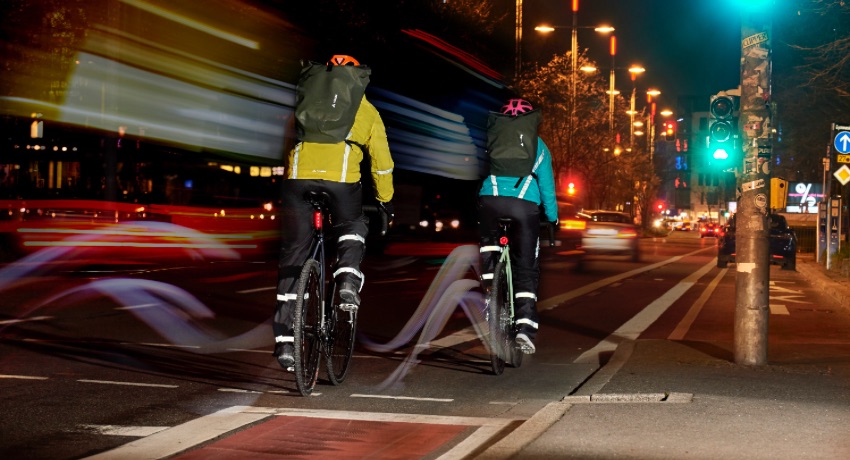 Deux cyclistes de dos pédale sur une bande cyclable urbaine de nuit avec leur éclairage et équipements d'hiver.
