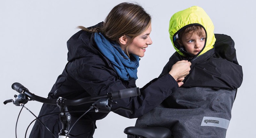 Un enfant sur un siège-bébé vélo revêt une cape de pluie thermique Tucano Urbano Opposum.