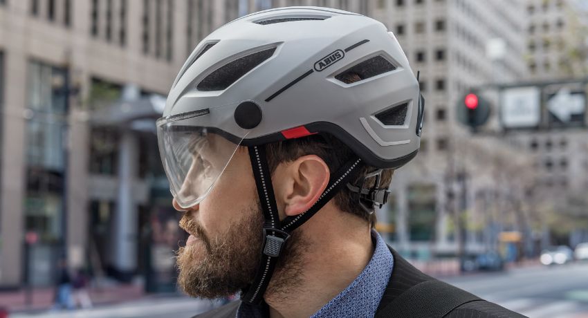 Un homme vu de profil en ville portant un casque Abus avec une visière écran panoramique et un système de réglage par molette.