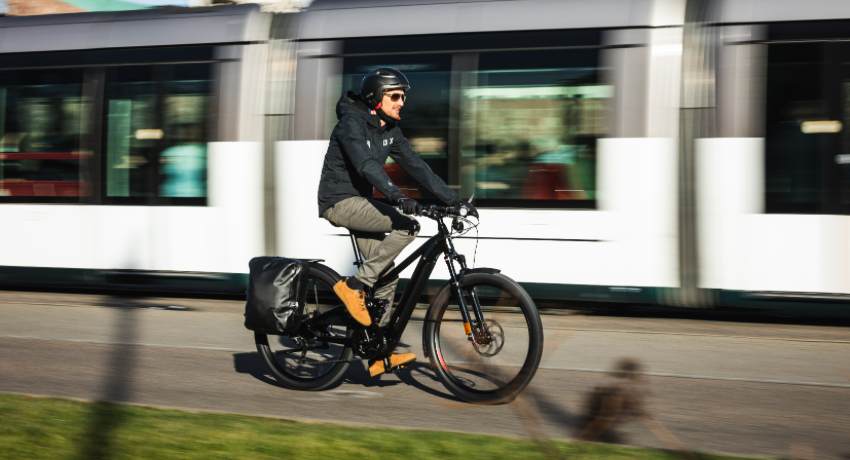 Un homme casqué roule à côté d'un tramway aux commandes d'un speedbike Moustache Friday 27 FS speed.