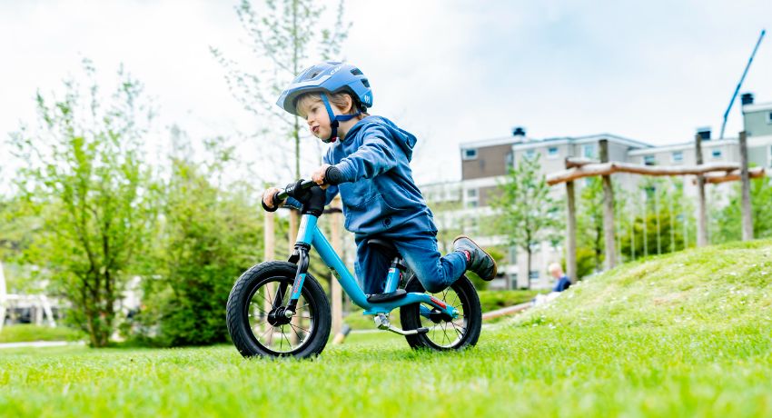 Un enfant sur une draisienne Puky descend une pente en herbe dans un parc.