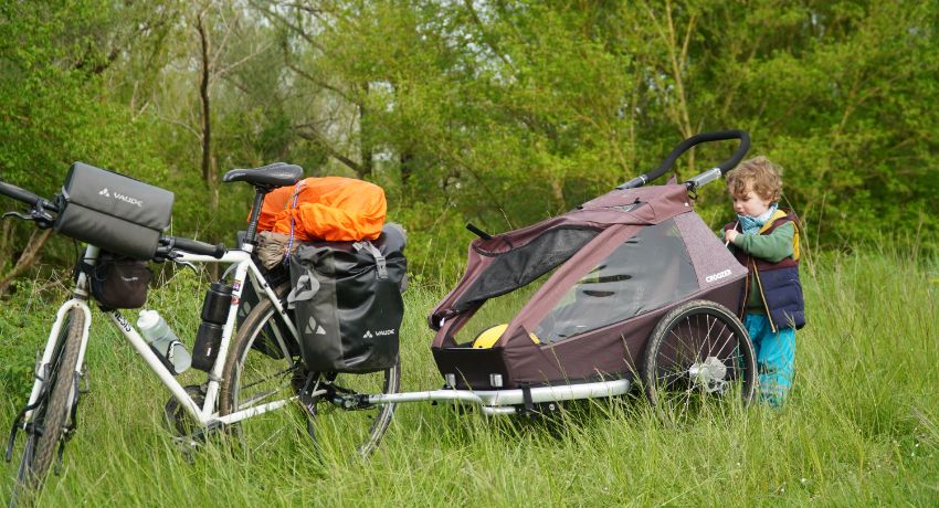 Une petite fille range le coffre de sa remorque vélo dans un environnement verdoyant.