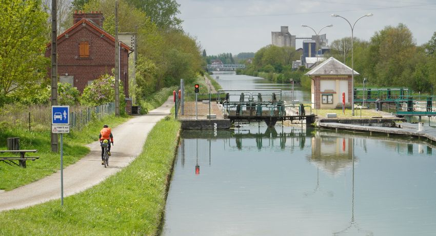 Un cycliste file sur une voie cyclable interdite aux voitures le long de canal.