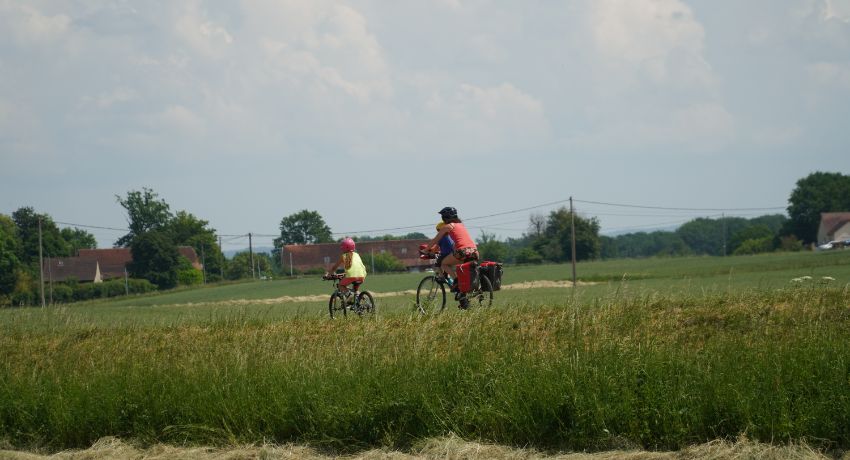 Une femme précédée d'une enfant à vélo progresse sur une voie verte à travers la campagne.