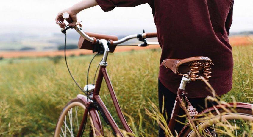 Une femme a mis pied à terre dans un champ avec son vélo équipé d'une selle Brooks montée sur ressorts.