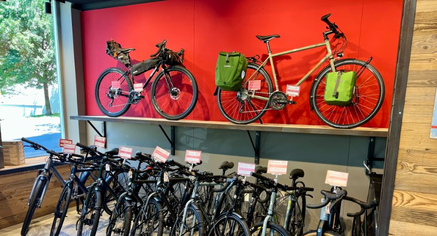 Un vélo de gravel équipé en bikepacking et un vélo de rando avec des sacoches latérales installés sur un présentoir au-dessus d'une large sélection de VAE.