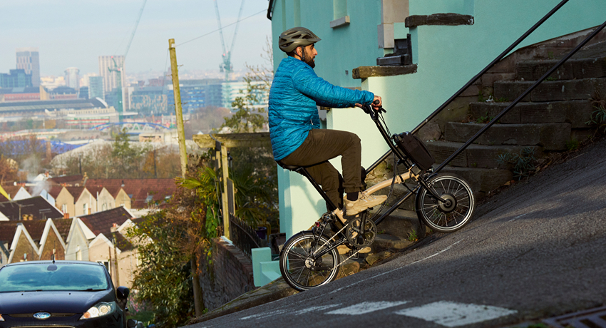 Un homme grimpe une pente très escarpée en ville grâce aux 12 vitesses du vélo électrique Brompton C Line en version Explore.