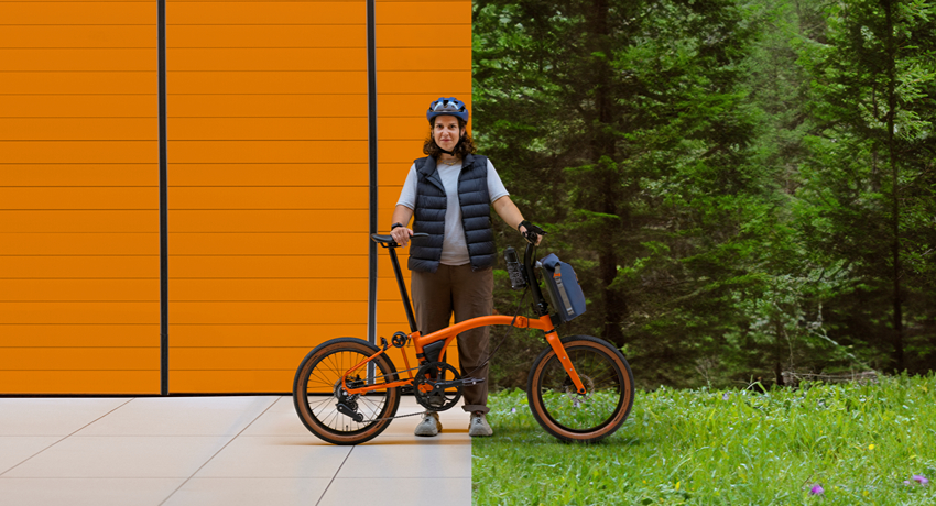 Une femme tient à la main un vélo pliant électrique Brompton G Line avec en toile de fond deux environnements : un urbain et l'autre forestier.